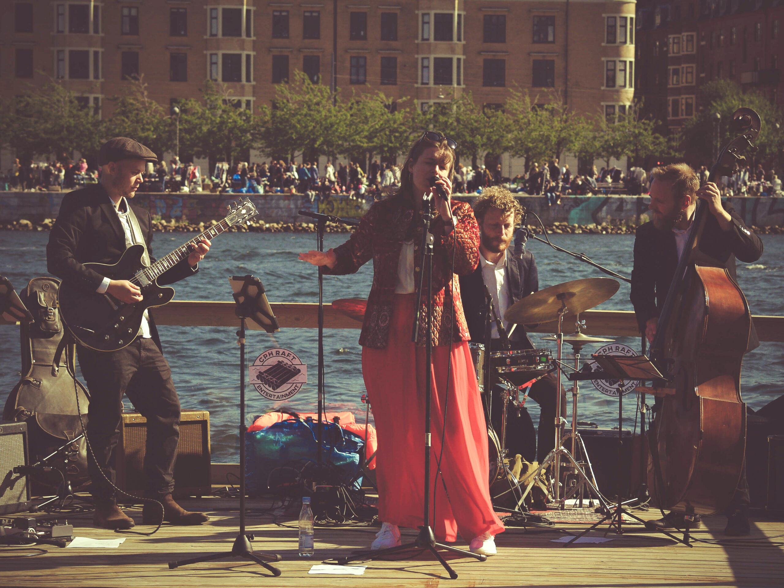 Det samme jazzbandet opptrer på en svevende scene, med fokus på sangeren i rød jakke og bukse.