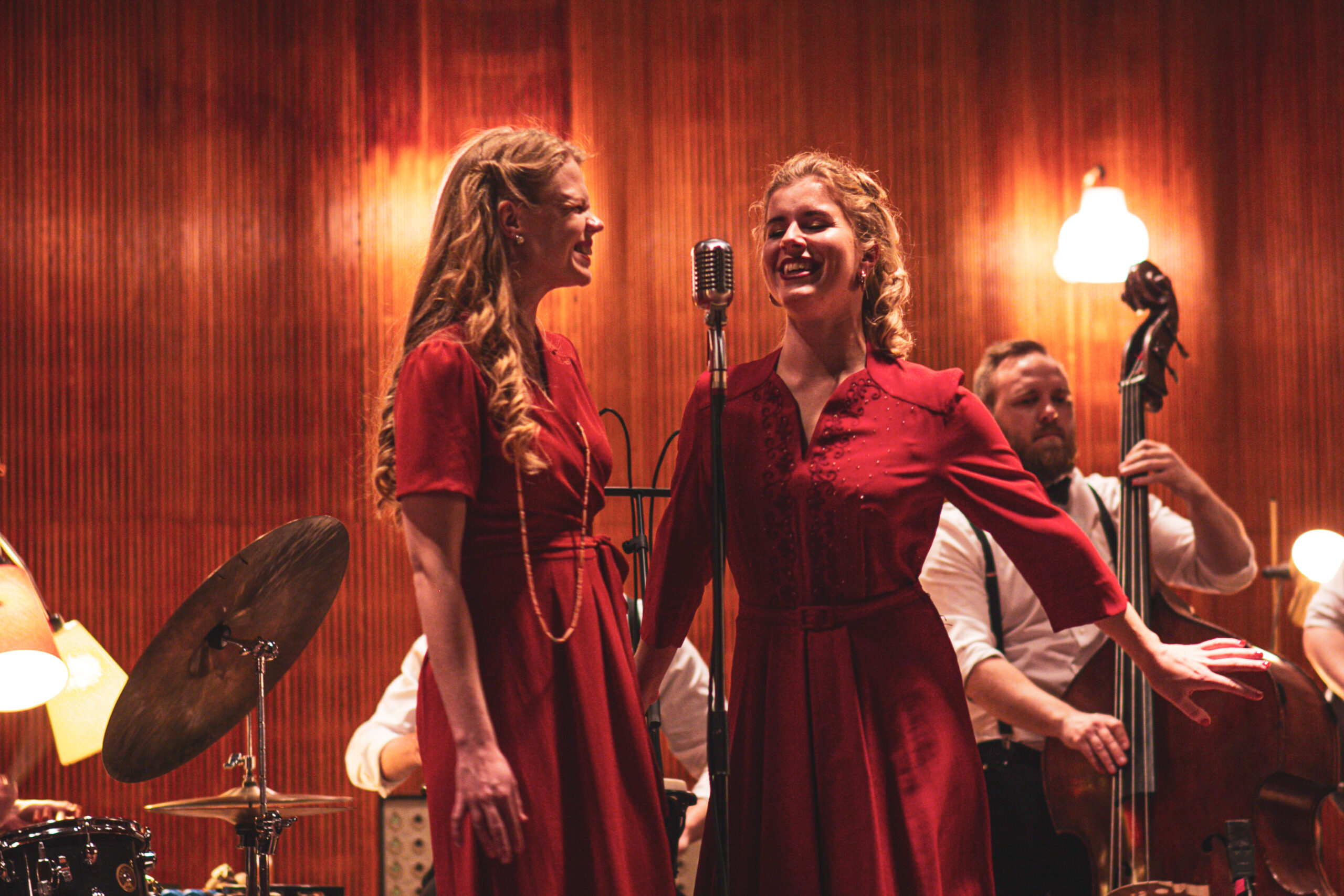 Två sångare i rött ler mot varandra under ett framträdande medan bandet bakom dem höjer stämningen med jazz och swing för bröllop