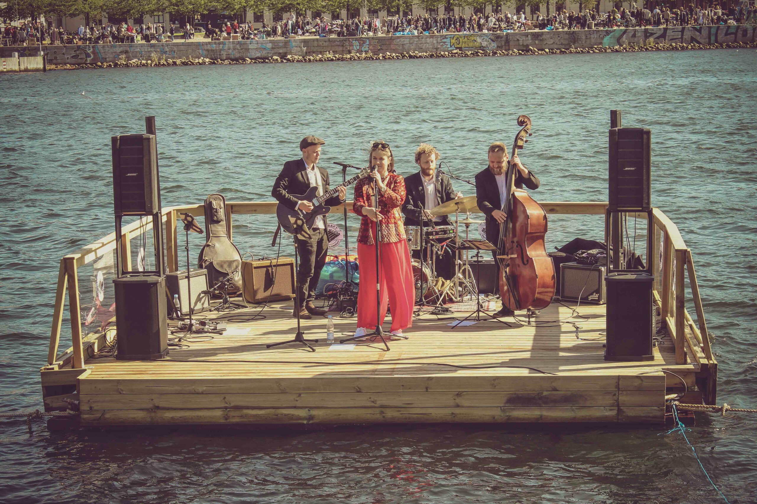 Drei Männer und eine Frau bilden eine Band, die auf einem schwimmenden Boot vor den Augen des Publikums spielt.