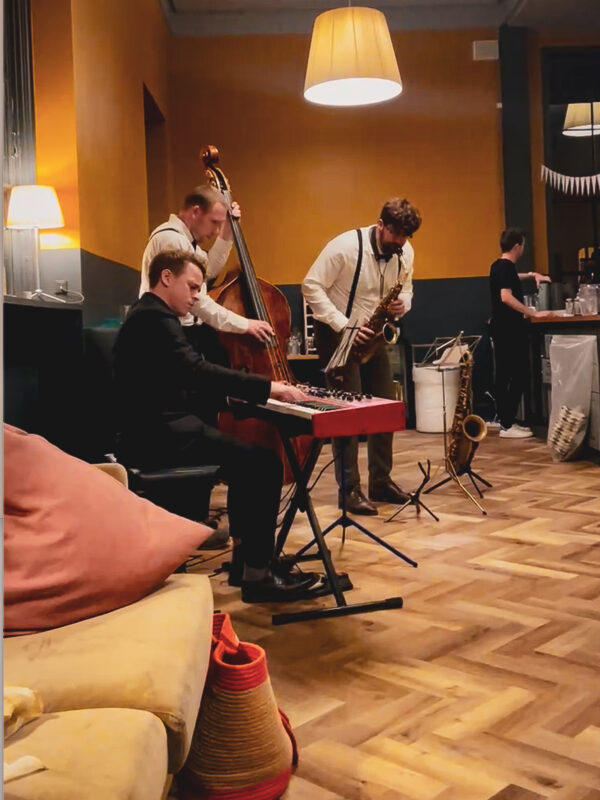 Three men form a trio where they gather around the music, with piano, double bass and saxophone playing