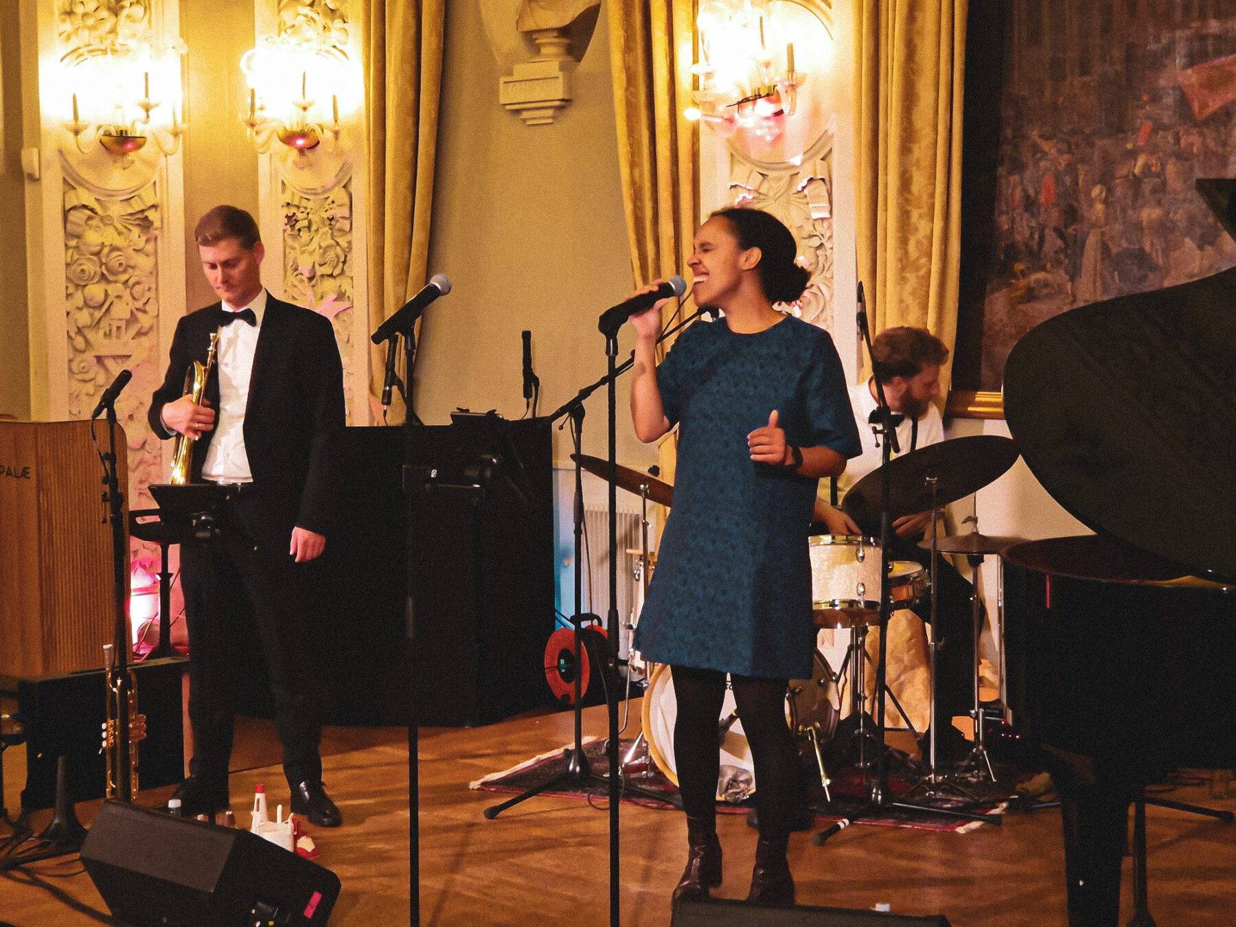 Sangerinden synger jazz med energi og nærvær, flankeret af trompetist og trommeslager, der driver rytmen frem til cocktailparty