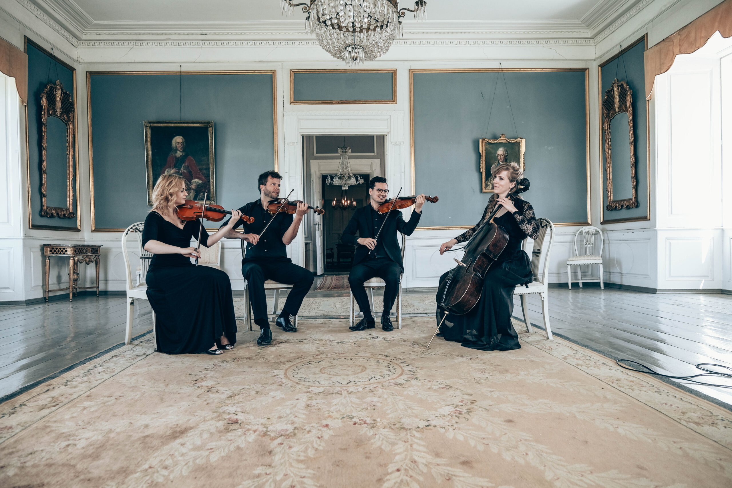 Strygerensemble poserer med violin, bratsch og cello i klassisk lokale til koncert eller bryllupsceremoni.