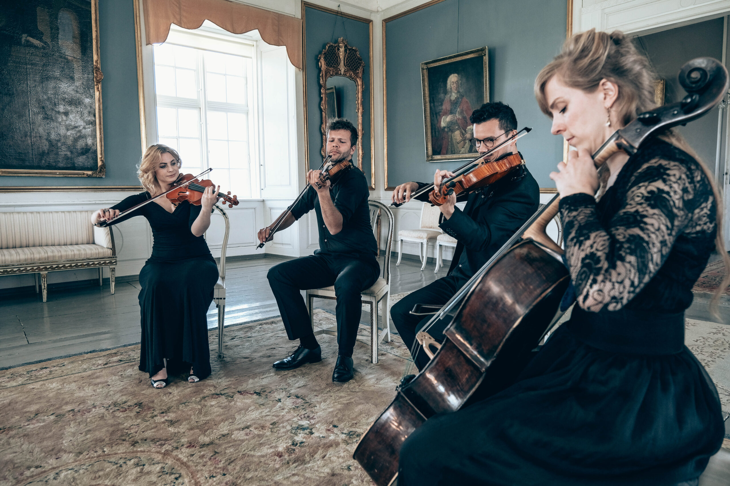 Strygekvartet spiller koncert i cirkelopstilling i historisk lokale med paneler og lysekroner.