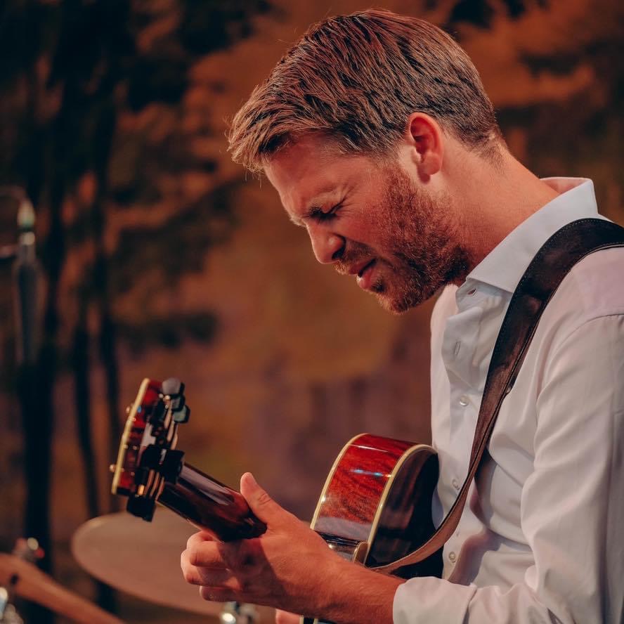 Mannen fordyper seg i lyden av gitaren, og intensiteten i ansiktet hans viser musikkens følelser i et øyeblikk av tilstedeværelse.