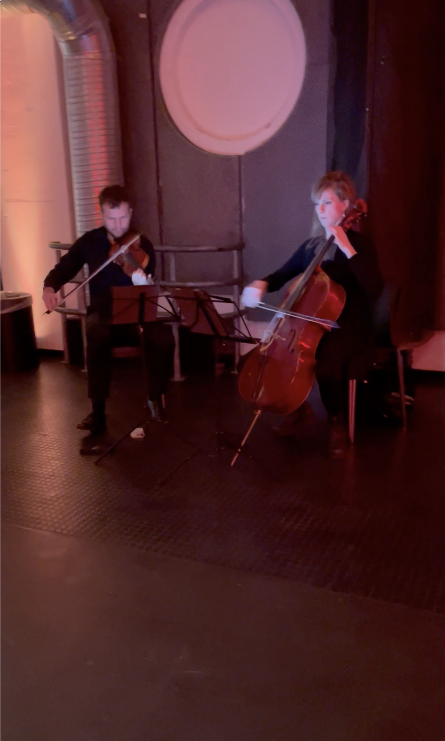 Klassisk duo med violin og cello spiller i stemningsfuldt lokale med rød og varm belysning til koncert eller privat selskab.