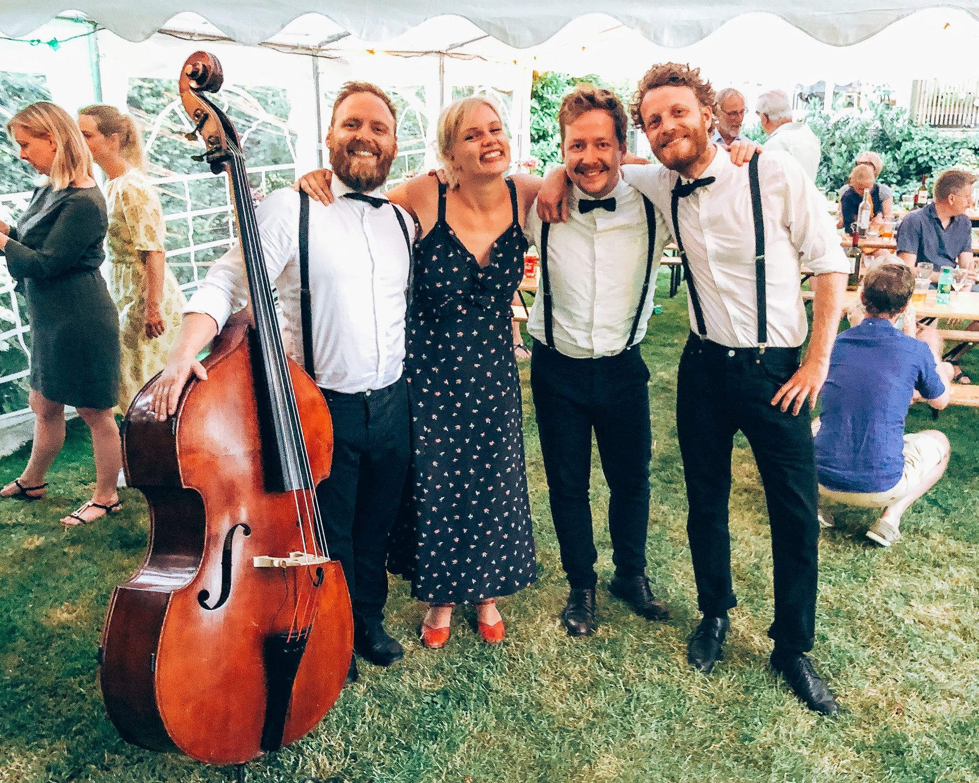 Four musicians smile together in tent during garden party where double bass, singing and live music create a festive atmosphere at private party