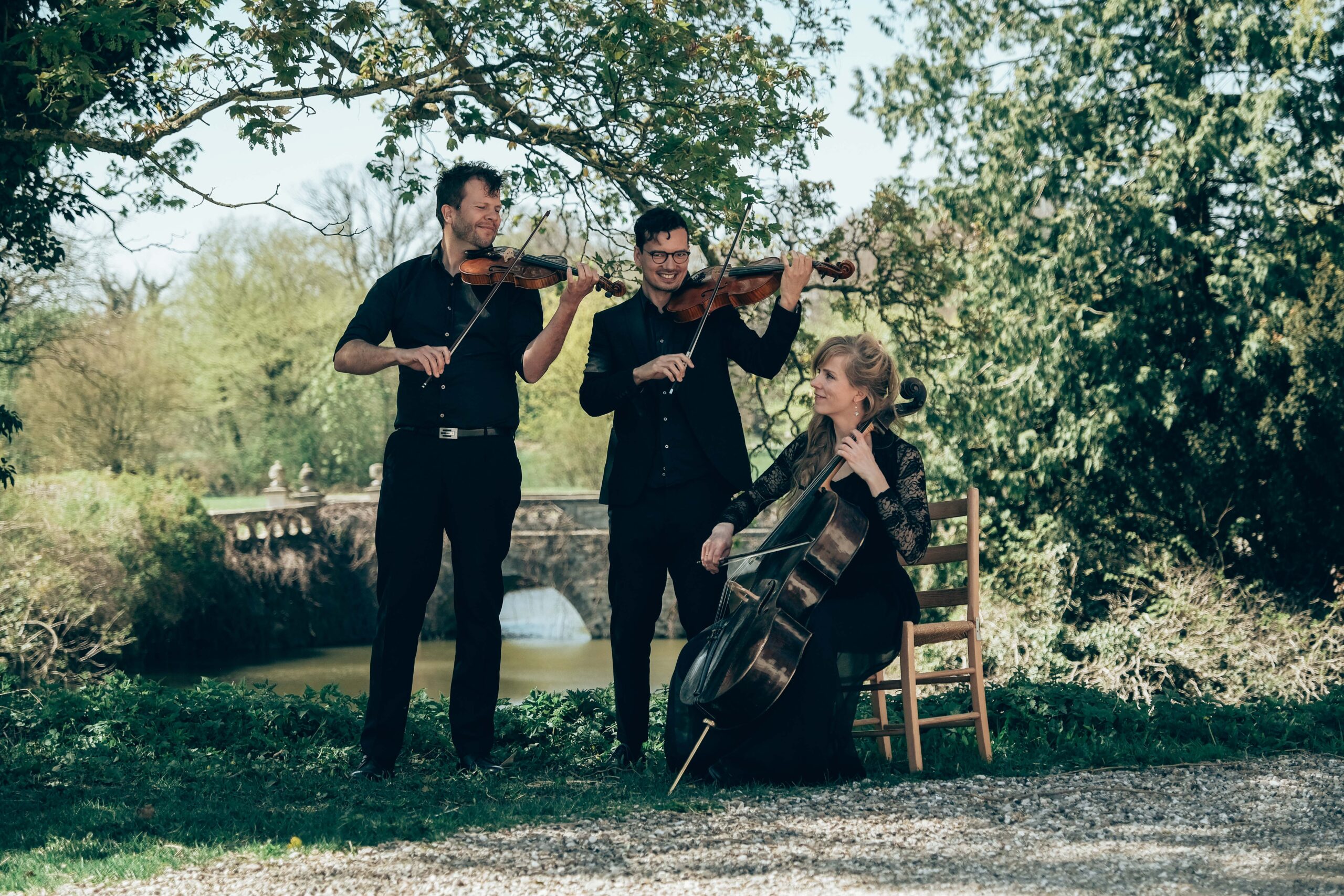 Klassisk trio med violin og cello spiller udendørs koncert i grønne omgivelser til vielse eller eksklusivt event.