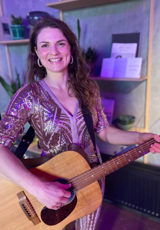 Kvindelig guitarist spiller akustisk guitar i farvet lys, hvilket skaber en intim og kreativ stemning med fokus på musik