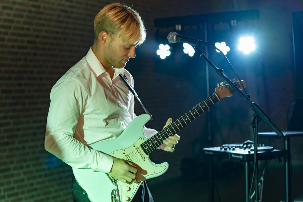 Elektrisk guitarist optræder i grønt scenelys med fokuseret kropssprog, hvilket understreger intensitet og liveperformance