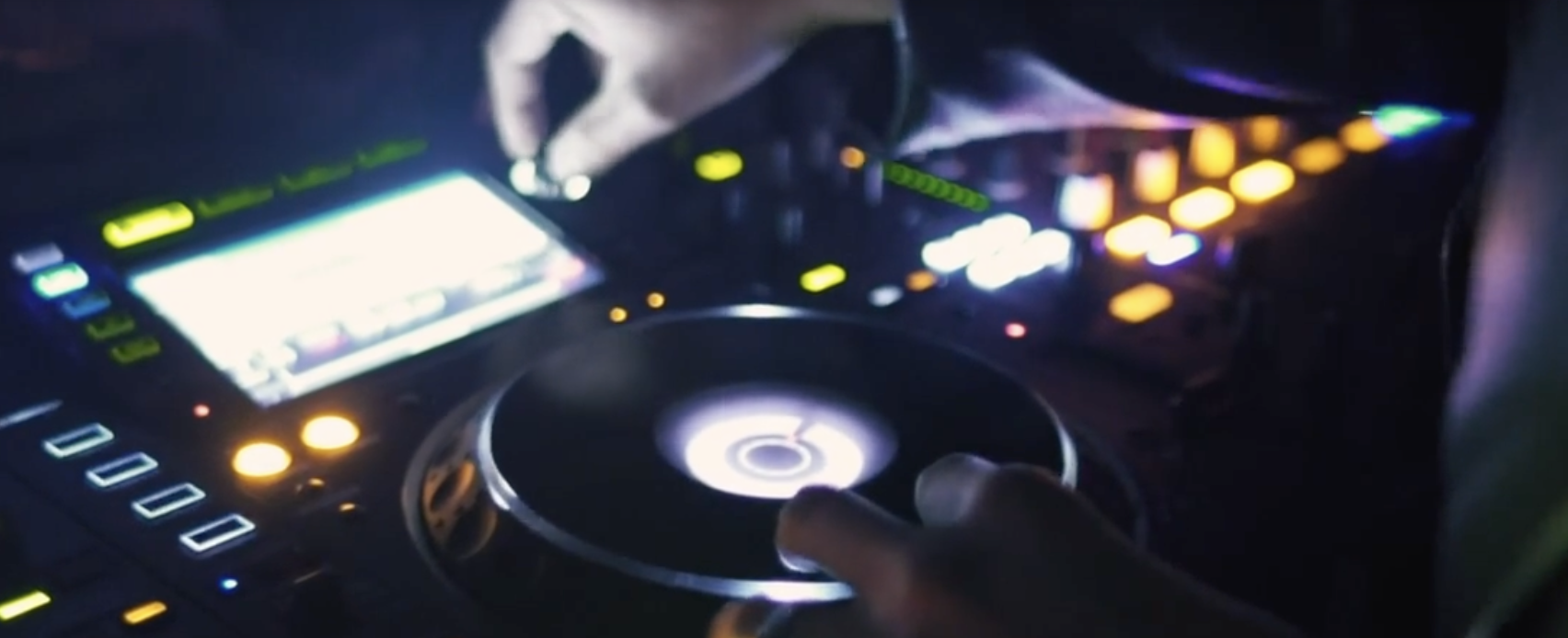 Nærbilde av DJ-pult med knotter og opplyste detaljer som fremhever musikkproduksjon, teknologi og atmosfæren i et live-oppsett