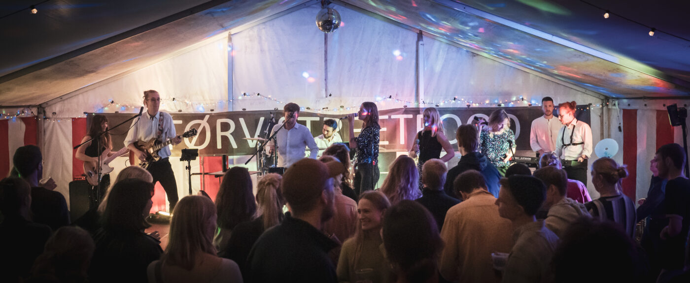 Audiences gather in front of the stage in a tent under the evening light, where live music and lighting create a festive and inclusive concert experience