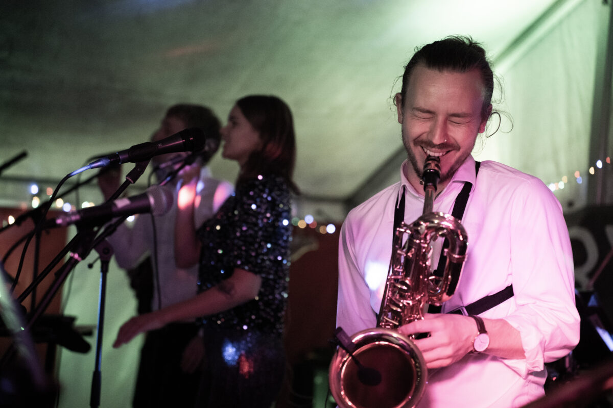 Saksofonisten spiller med stort engasjement under liveopptredener, fanget i bevegelse med scenelys som fremhever energi og musikalsk dynamikk