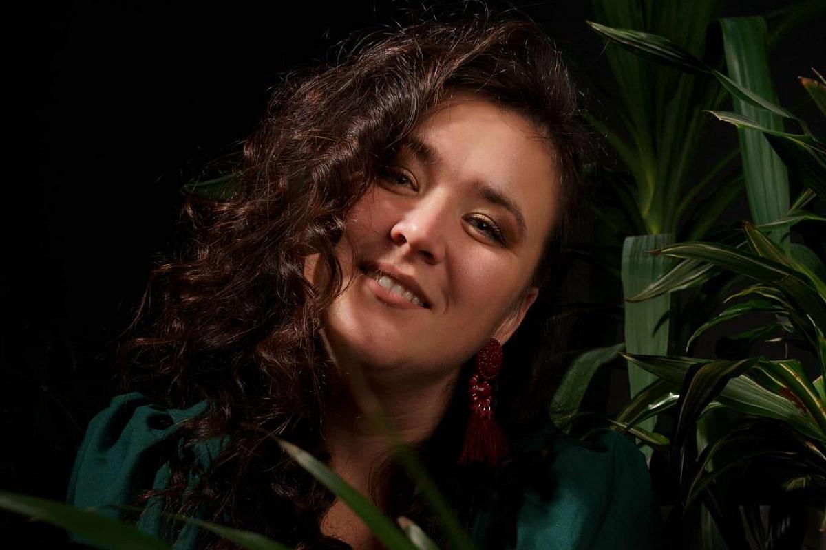 Porträtt av kvinna med lockigt hår i mjukt, naturligt ljus och grön bakgrund, vilket skapar ett intimt och konstnärligt uttryck med fokus på närvaro