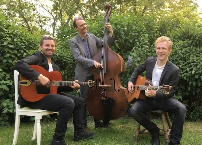 Akustisk trio spelar gitarr och kontrabas i gröna omgivningar och skapar en varm och levande atmosfär med fokus på interaktion
