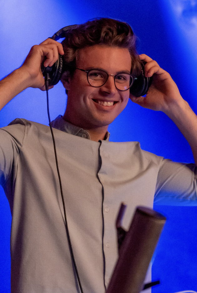 Ung DJ justerer hovedtelefoner foran farvet baggrund og professionelt udstyr, hvilket signalerer musikproduktion, fokus og moderne kreativ performance