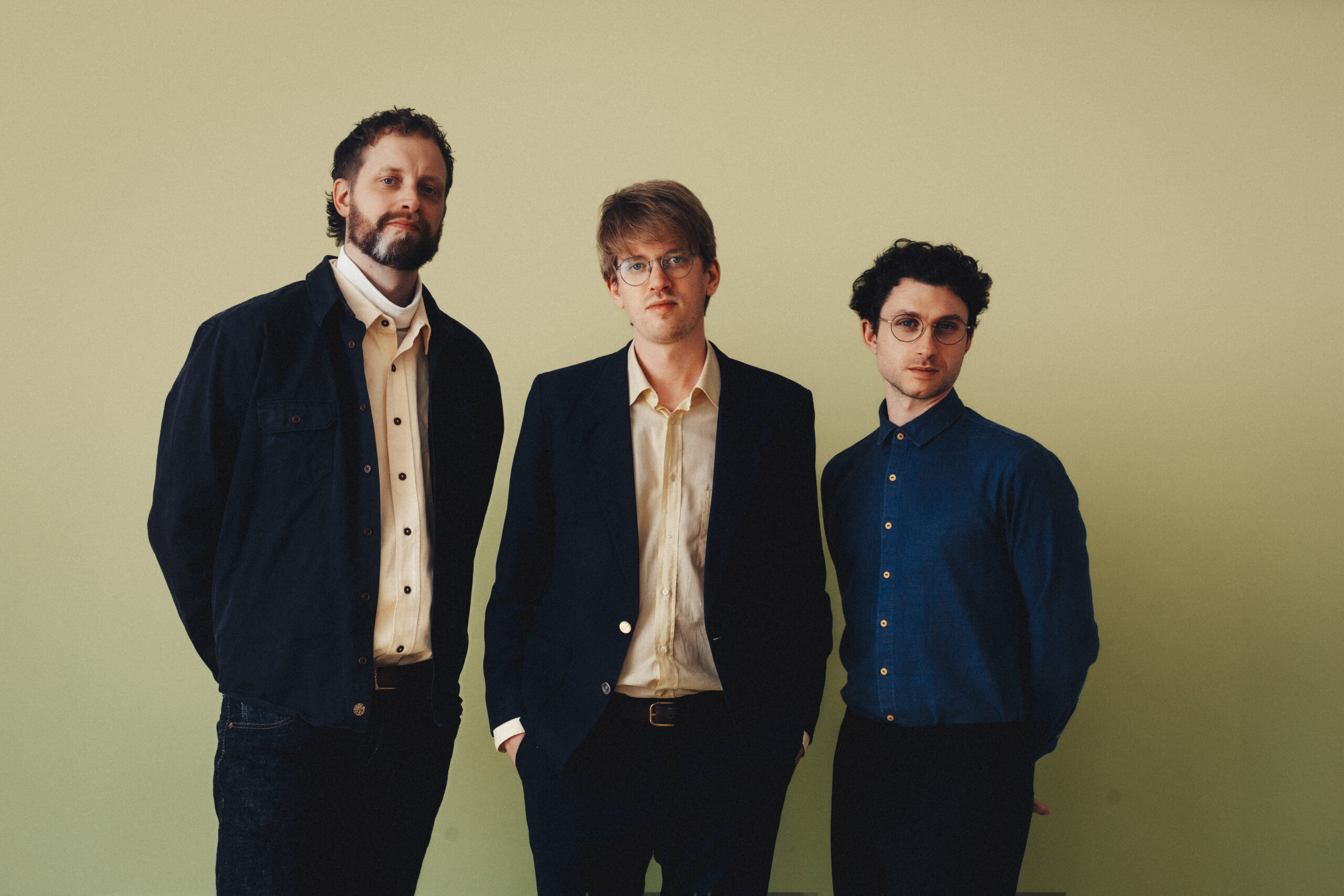 Tre menn i elegante, moderne antrekk står foran en nøytral bakgrunn og skaper et profesjonelt og stilfullt portrett med personlighet