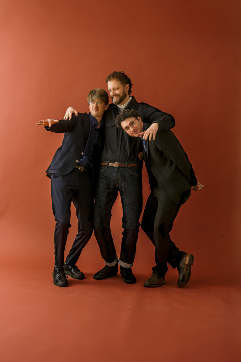 En gruppe menn beveger seg energisk mot kameraet mot en farget bakgrunn, noe som skaper et dynamisk og lekent visuelt uttrykk