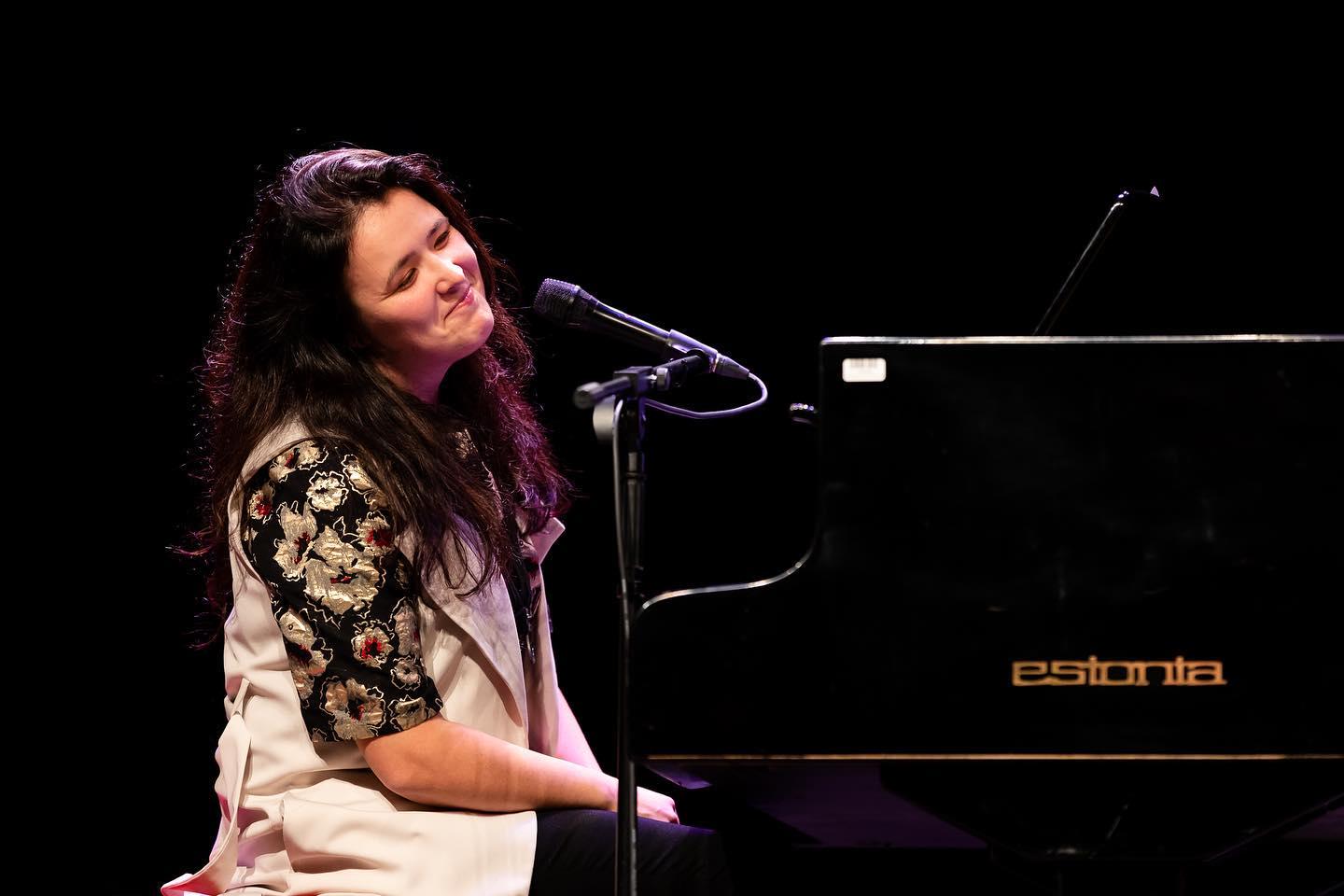 Sångerskan sjunger vid pianot i svagt ljus med känsligt uttryck, vilket skapar en intim och känslomässig musikupplevelse